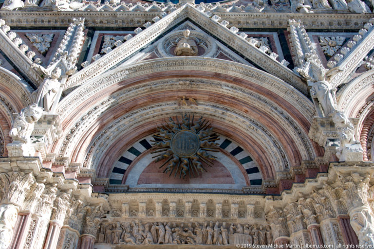 The cathedral’s oval window sits above a carved gallery of figures and striped marble bands.