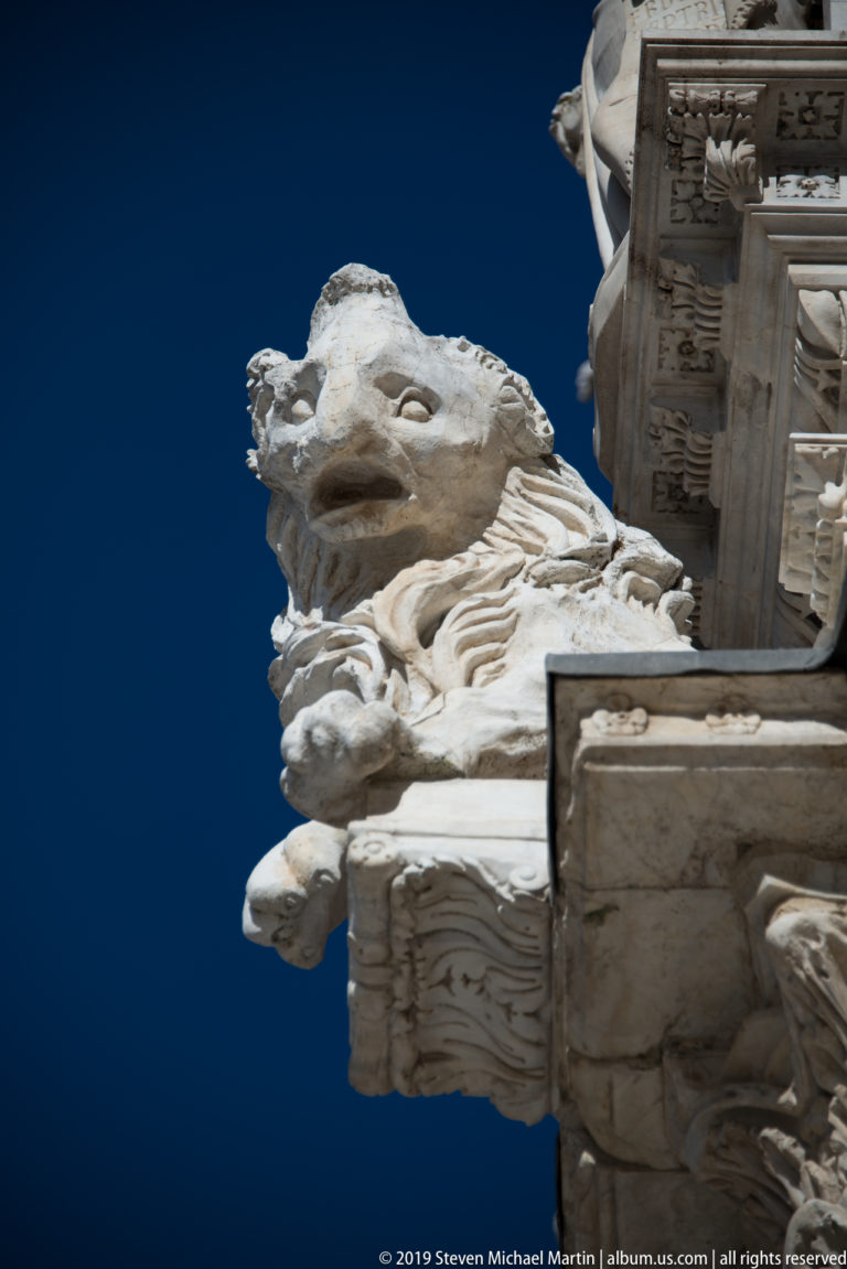 A weathered animal-like stone carving projects from the cathedral wall against a deep blue sky.