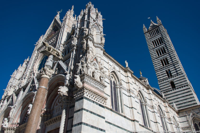 Low-angle view of Siena Cathedral’s sculpted white façade beside its striped campanile.