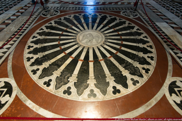 A circular marble floor design radiates from a central figure in alternating dark and pale bands.
