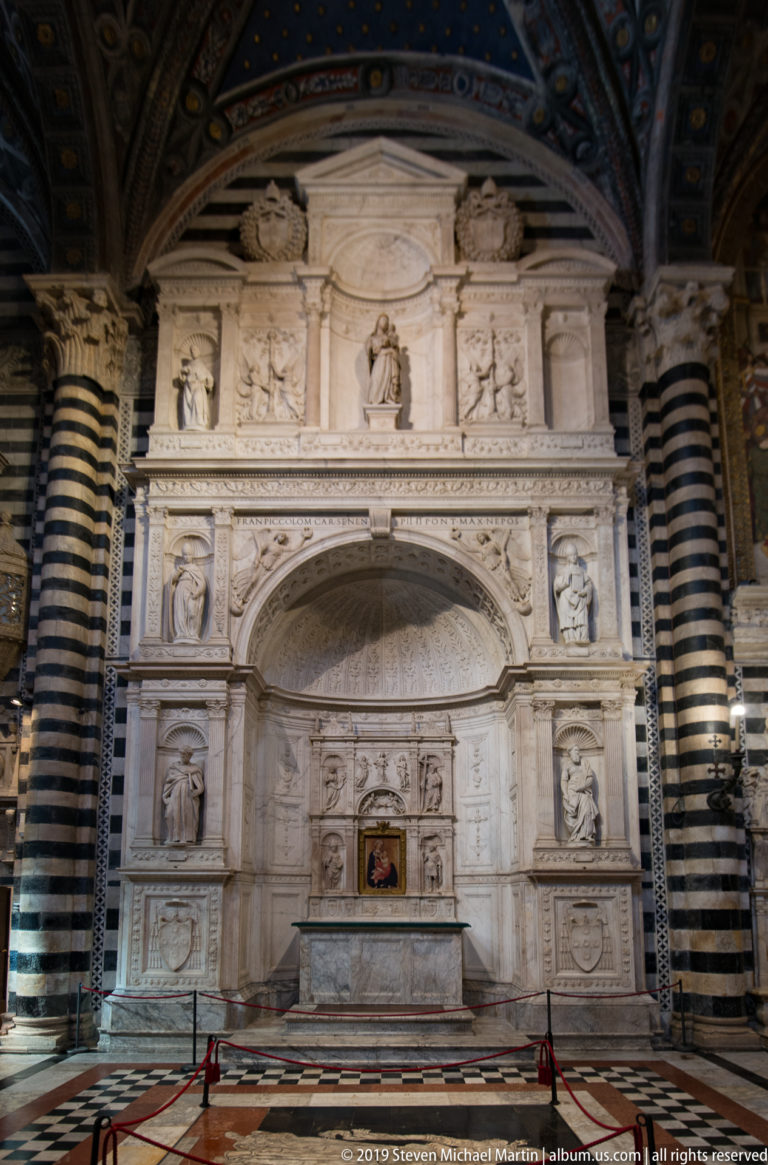 A pale marble altar screen with reliefs, small statues, and a central devotional image.