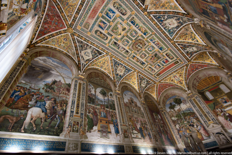 A steep view links the cathedral’s painted vaults with a crowded inlaid floor panel and visitors.