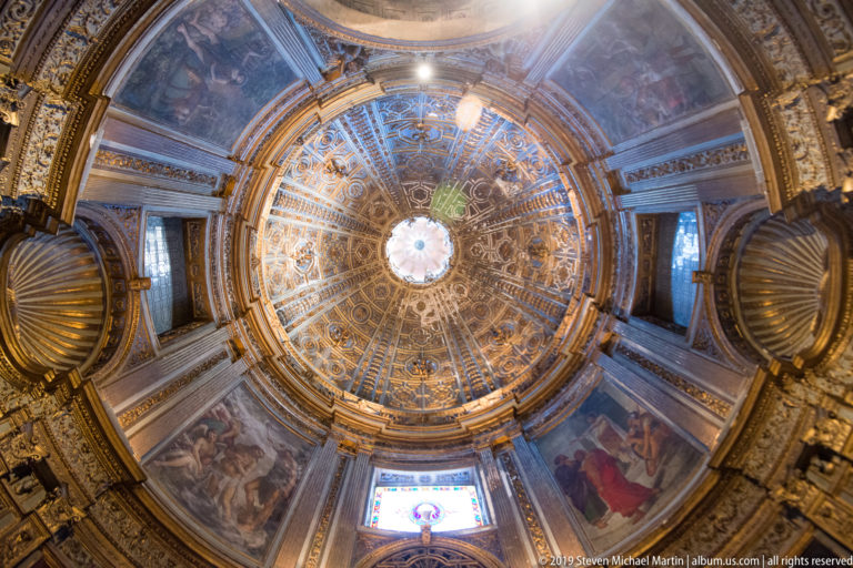 A gilded circular ceiling bay with painted panels and a bright central opening above the nave.
