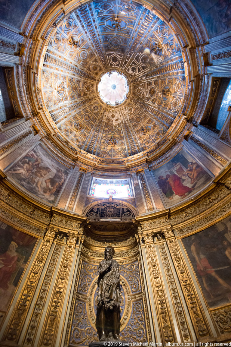 A gilded oval ceiling surrounds a bright central medallion above a small altar and blue wall panel.