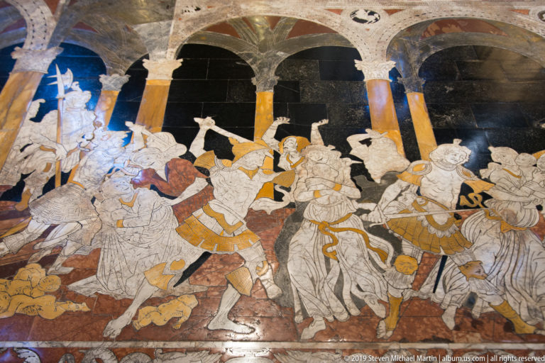 A marble floor panel with a procession of outlined figures in pale, ochre, and dark inlay.