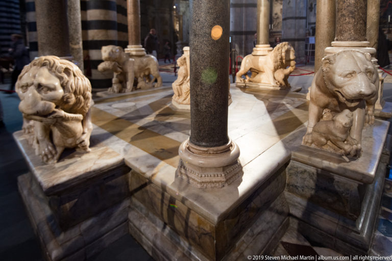 Marble lions surround the base of a dark column on a stepped pulpit platform.