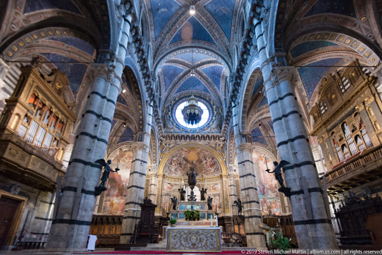 A carved marble pulpit structure with sculpted figures and pointed arches inside Siena Cathedral.