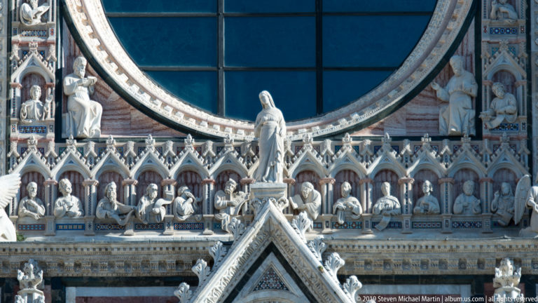 Stone figures line repeated pointed niches, with a larger robed statue at the center.