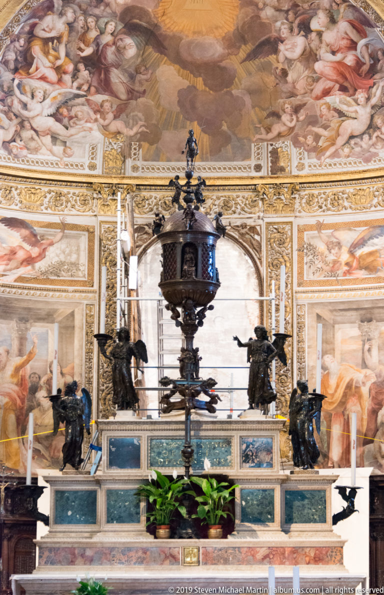 A dark hanging lamp before a richly painted and gilded wall inside Siena Cathedral.