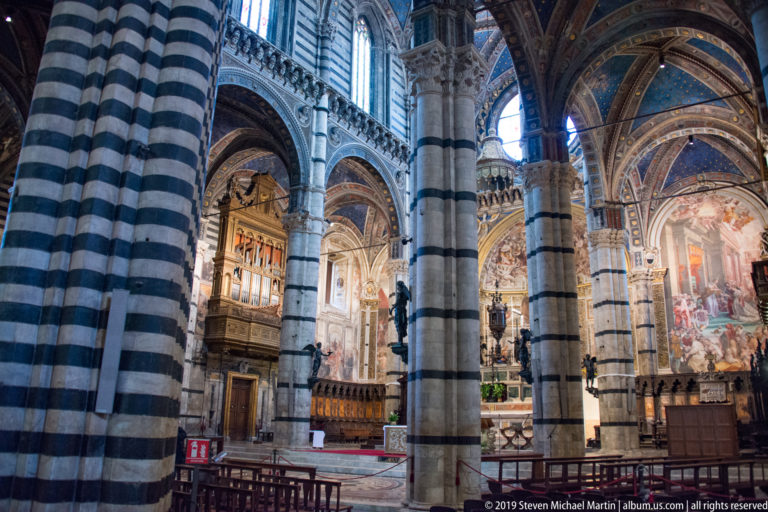 Striped stone columns frame a distant altar and painted sanctuary inside Siena Cathedral.