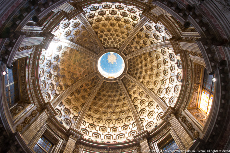 A circular blue medallion at the center of an ornate gold and cream octagonal cathedral ceiling.
