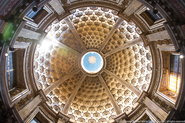 Overhead view of an ornate octagonal ceiling bay with gold geometric panels and a blue central medallion.