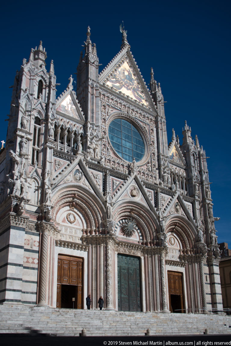 The central portal of Siena Cathedral framed by carved arches, striped marble, and the oval window above.
