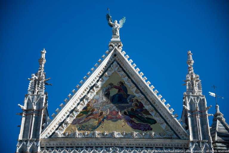 A gold-ground religious scene fills a triangular gable beneath a statue at its apex.
