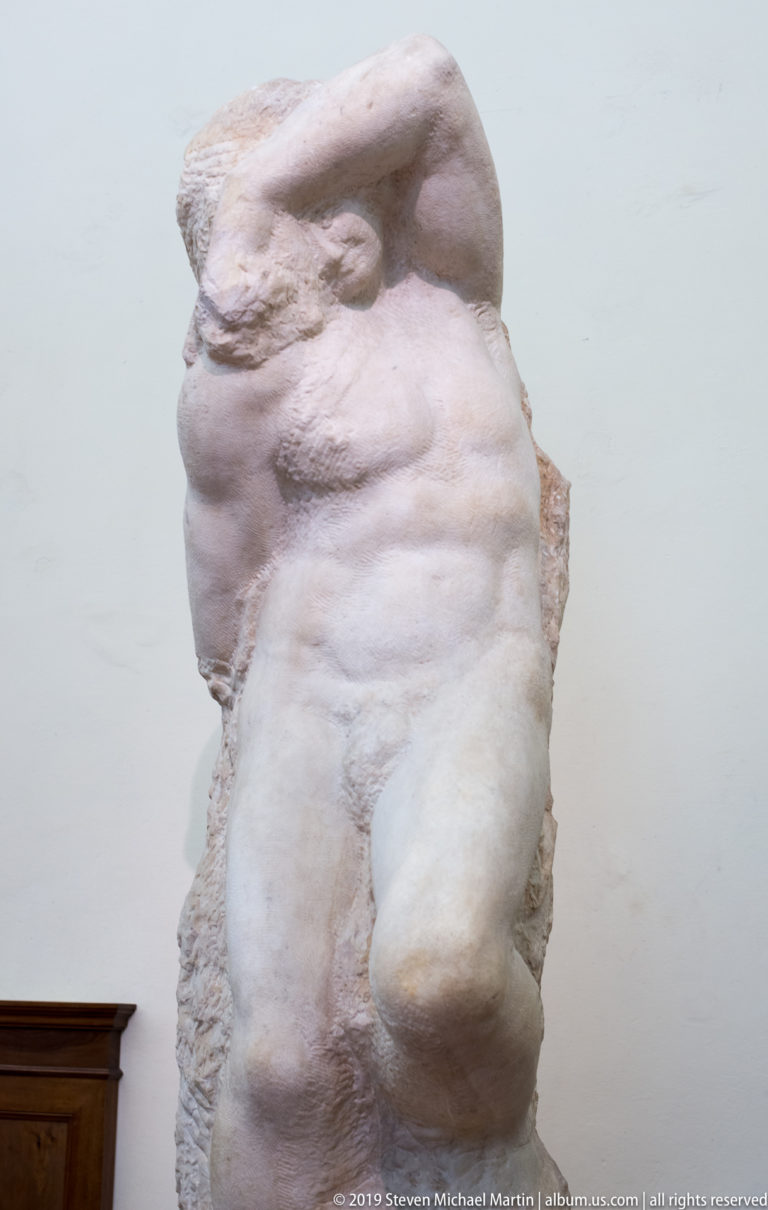 Close frontal detail of Michelangelo’s Atlas Slave showing modeled abdomen and leg emerging from a broad rough marble block.