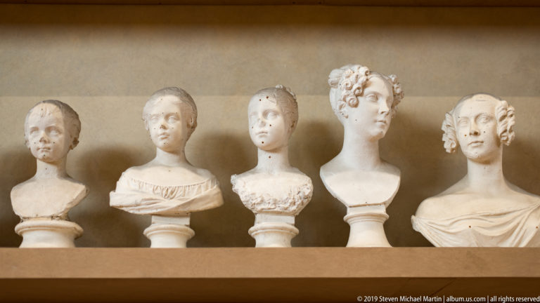 Five pale female portrait busts arranged in a row, each with distinct hairstyle, clothing, and pedestal.