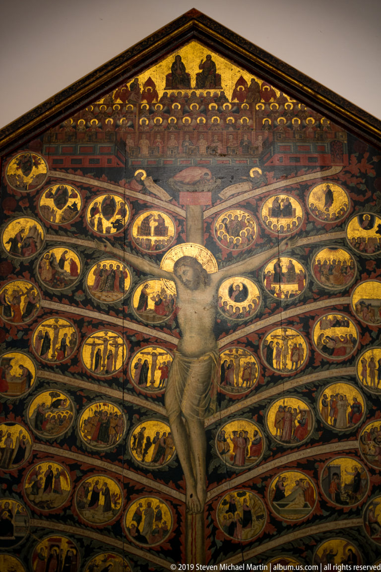 Large gabled Tree of Life painting with the crucified Christ at center and many gold narrative roundels branching around him.