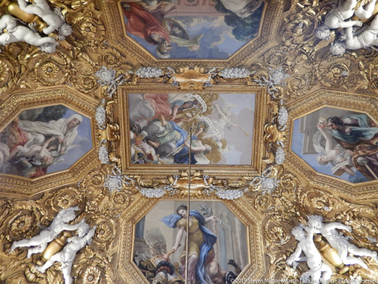 Ornate palace ceiling with painted compartments, gilded relief, and sculptural decoration.