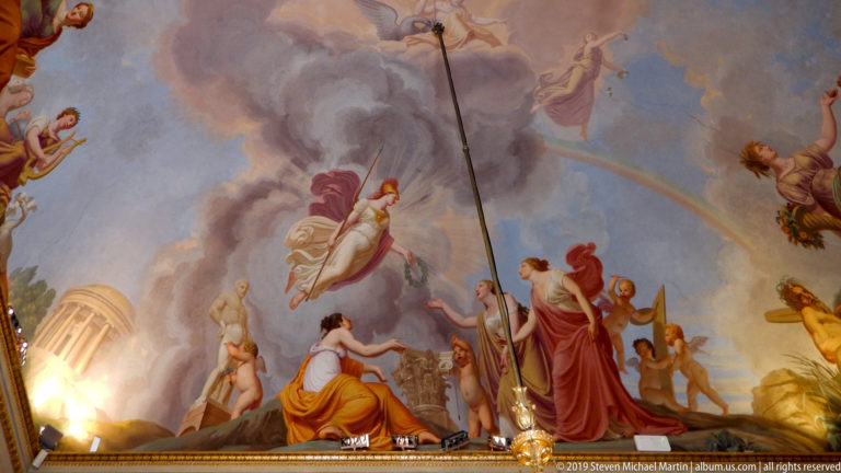 Ornate palace ceiling with painted compartments, gilded relief, and sculptural decoration.