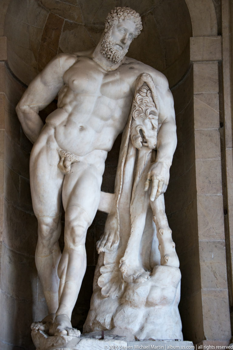 Close view of a white marble group with a muscular standing nude beside a slumping draped figure.
