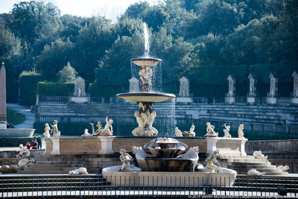 Sculptural fountain with water basins, statues, terraces, and formal garden landscaping.