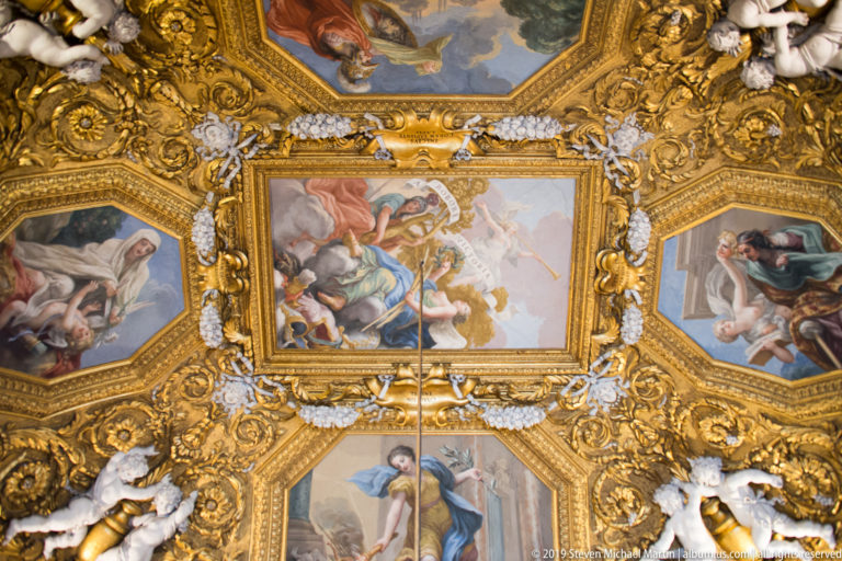 Ornate palace ceiling with painted compartments, gilded relief, and sculptural decoration.