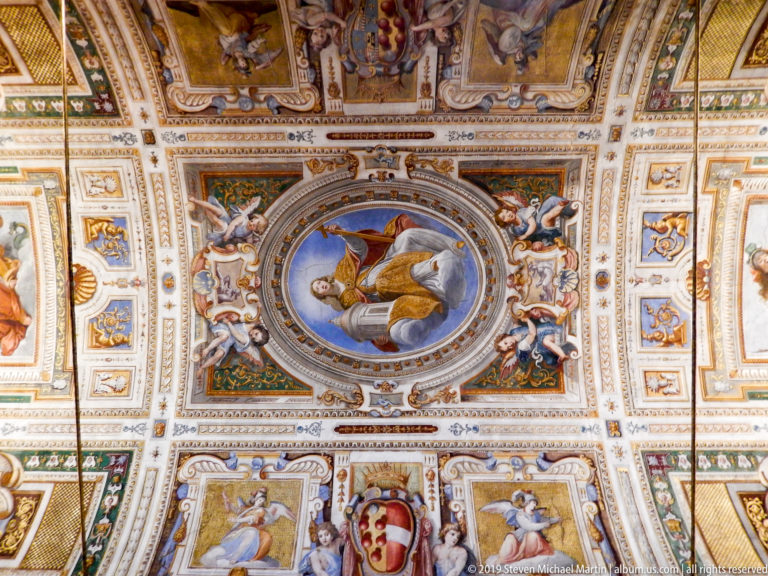 Ornate ceiling with central oval reclining figure, heraldic shield, small painted figures, grotesque ornament, and intricate borders.