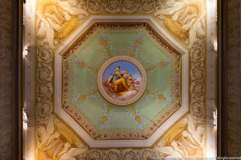 Pale green octagonal ceiling panel with central painted female figure, floral garlands, gilded details, and cream relief borders.