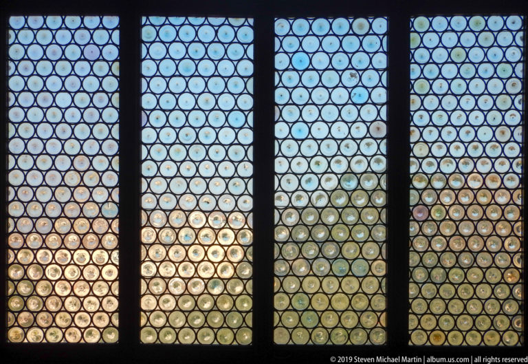 Four tall window panels filled with small circular leaded panes, with trees and landscape visible through the glass.