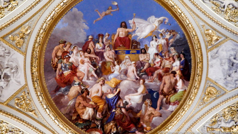 Circular ceiling fresco with many mythological figures gathered around a central enthroned deity against blue sky.