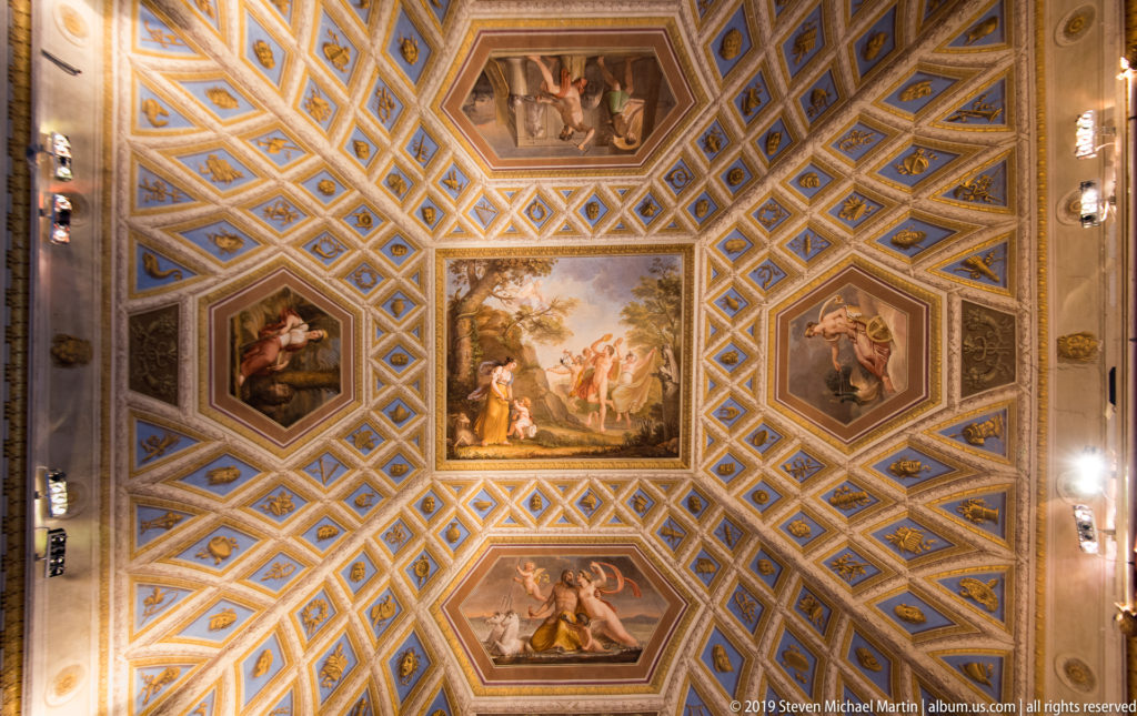 Blue-and-gold geometric coffered ceiling with a central square painting and four surrounding figurative panels.