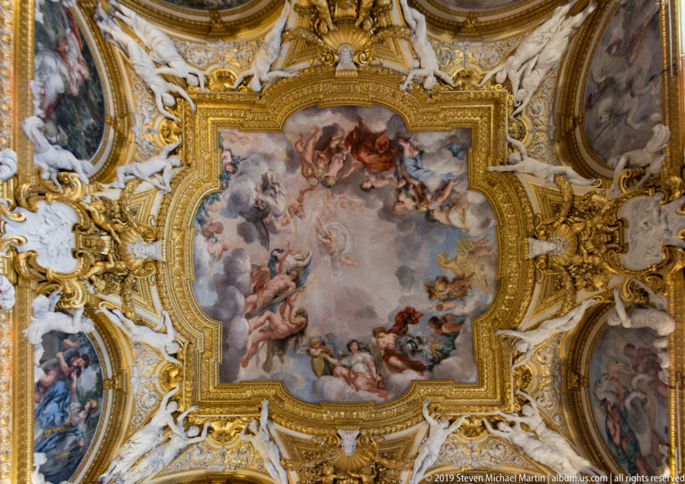 Broad fresco of figures in clouds enclosed by scalloped gilded frame and surrounding painted medallions.