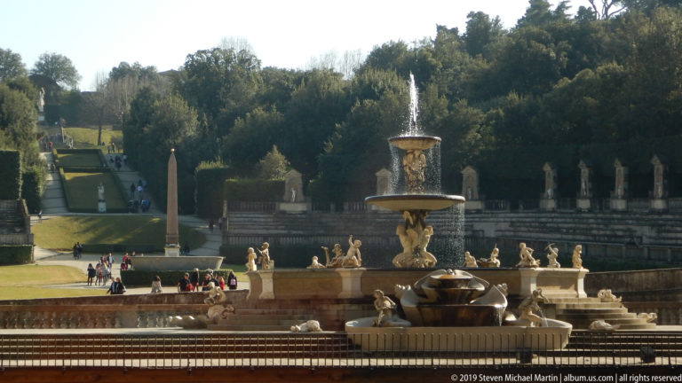 Sculptural fountain with water basins, statues, terraces, and formal garden landscaping.
