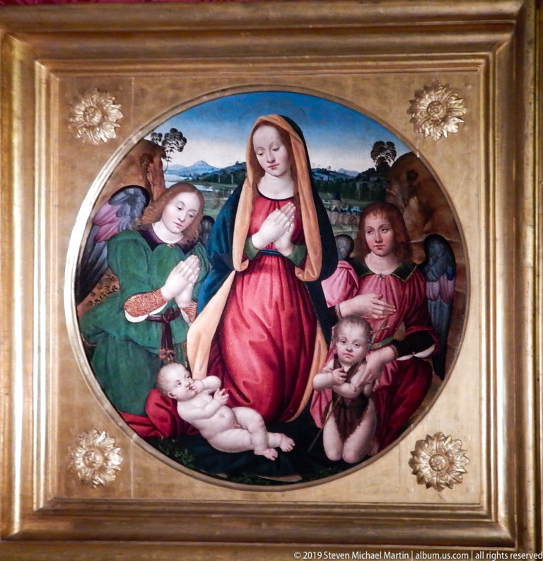 Oval religious painting shows a red-robed Virgin, reclining infant and two winged angels against a distant landscape.