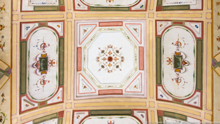 Pastel vaulted ceiling with an octagonal floral rosette, long oval ornamental panels, grotesque figures, and geometric borders.