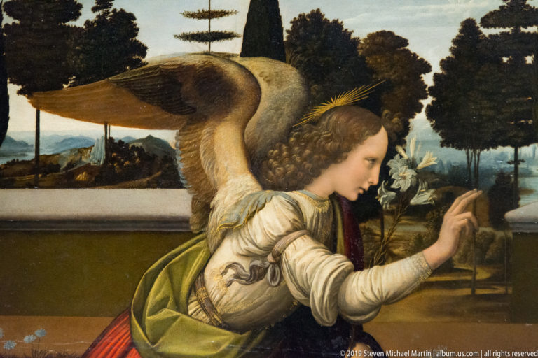 Detail of Leonardo’s Annunciation showing the kneeling Archangel Gabriel holding lilies in a flowering enclosed garden.