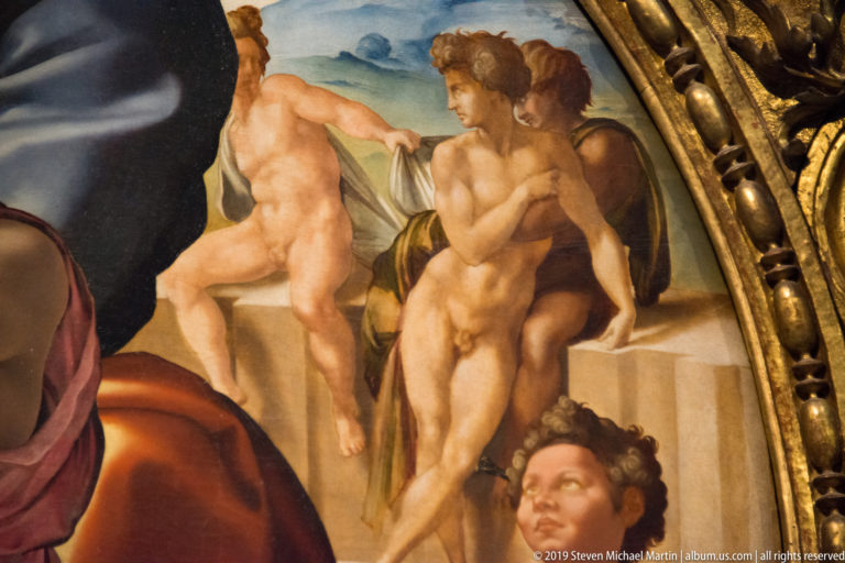 Detail of Michelangelo’s Doni Tondo showing nude youths in the rocky background beside the carved gilded circular frame.