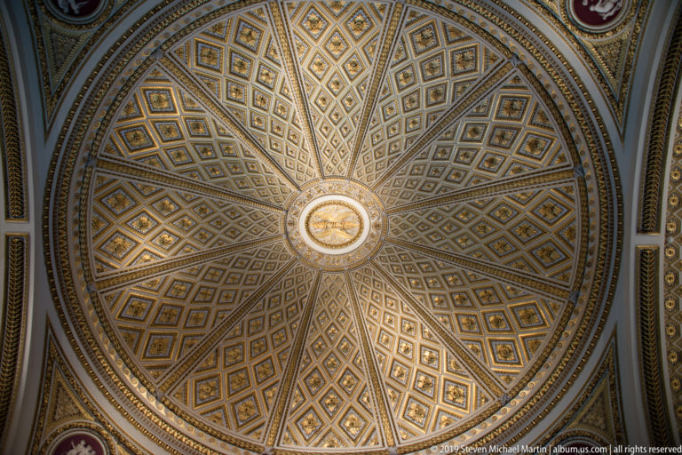 Ornate vaulted ceiling with radiating geometric coffers, gilded details, and a circular central medallion.