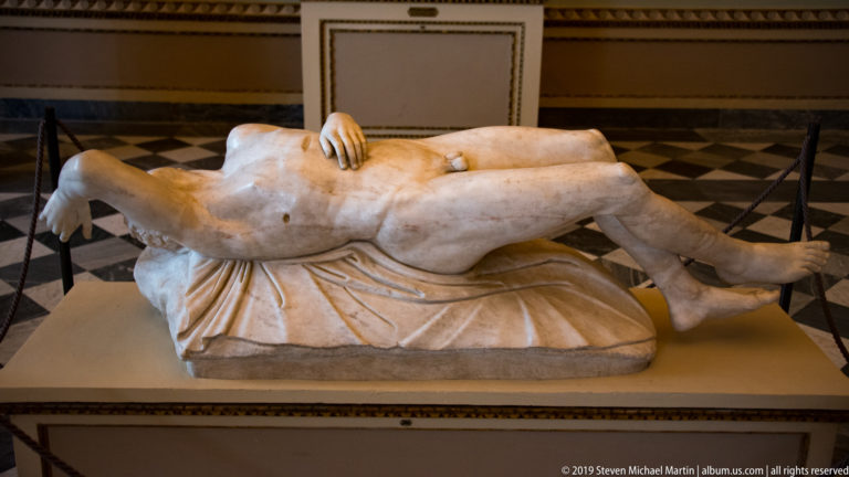 Headless reclining marble nude with crossed legs and one hand resting on the abdomen.