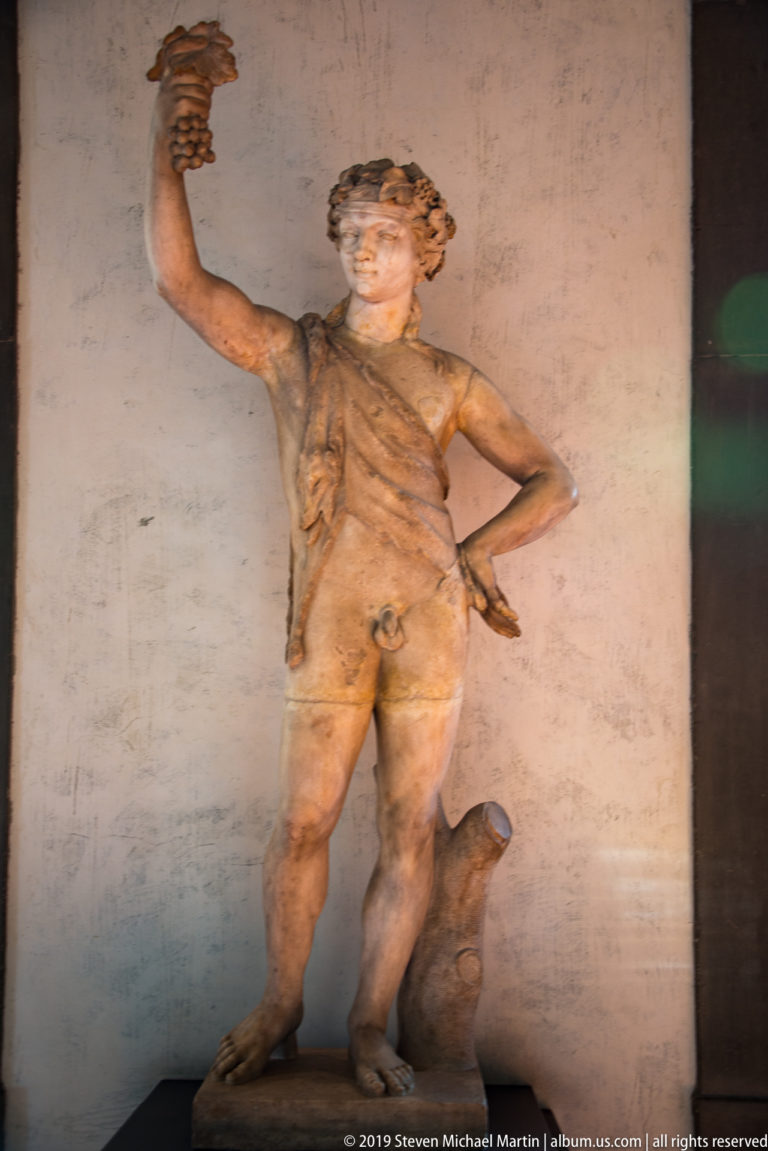 Marble statue of a youthful nude figure with an outstretched arm and a support beside one leg.
