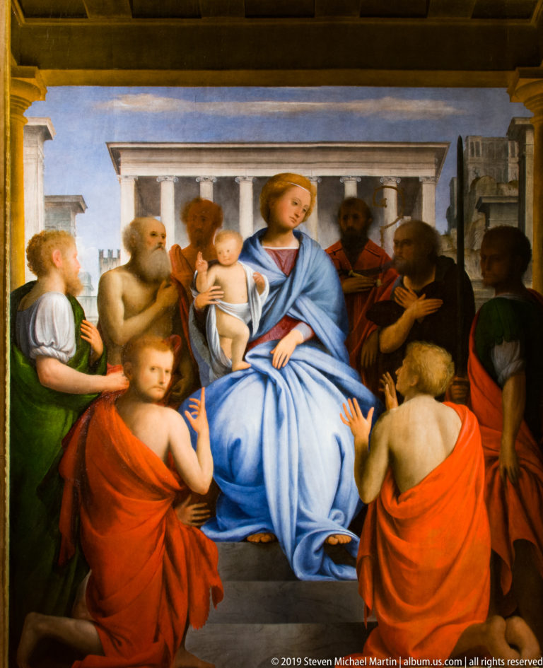 Enthroned Virgin in blue holding the infant Christ, surrounded by standing and kneeling saints.