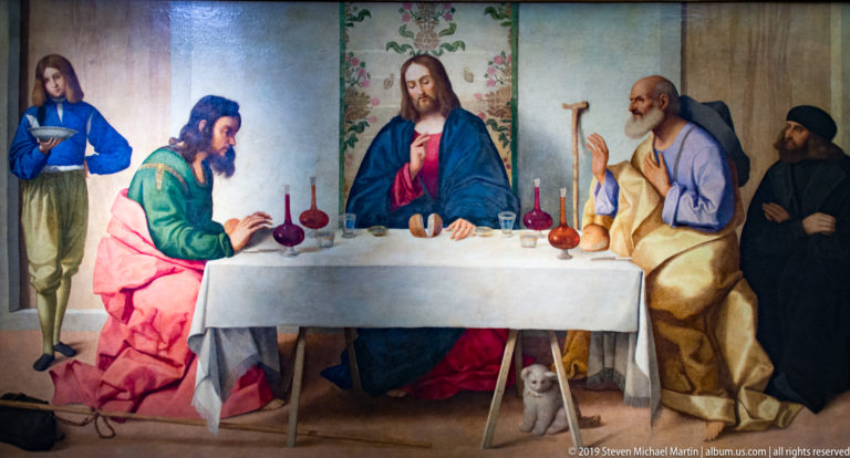 Christ seated at a white-covered table with disciples and attendants, with wine vessels and a small dog below.