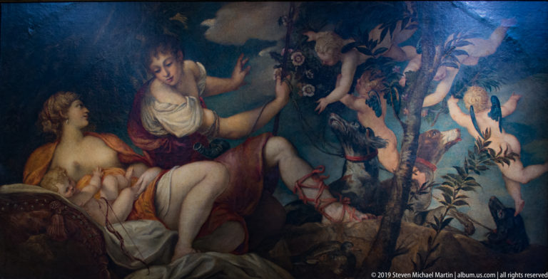 Two reclining women beneath trees with small winged figures and flowers in a dark wooded setting.
