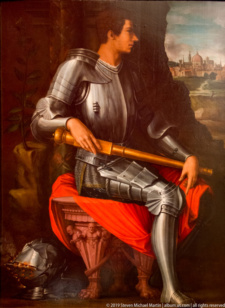 Seated man in plate armor holding a baton, with red drapery and a distant Florentine skyline.