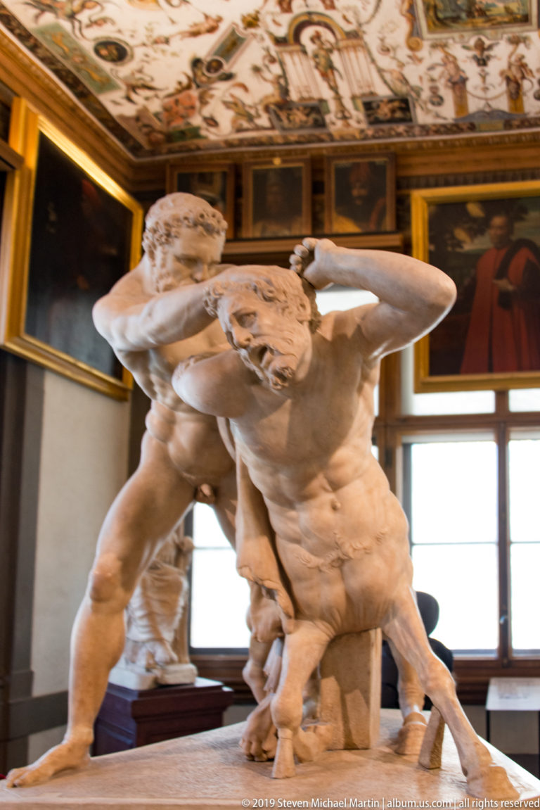 Two nude marble wrestlers grapple in a twisting group, one bent forward while the other braces across his shoulders.