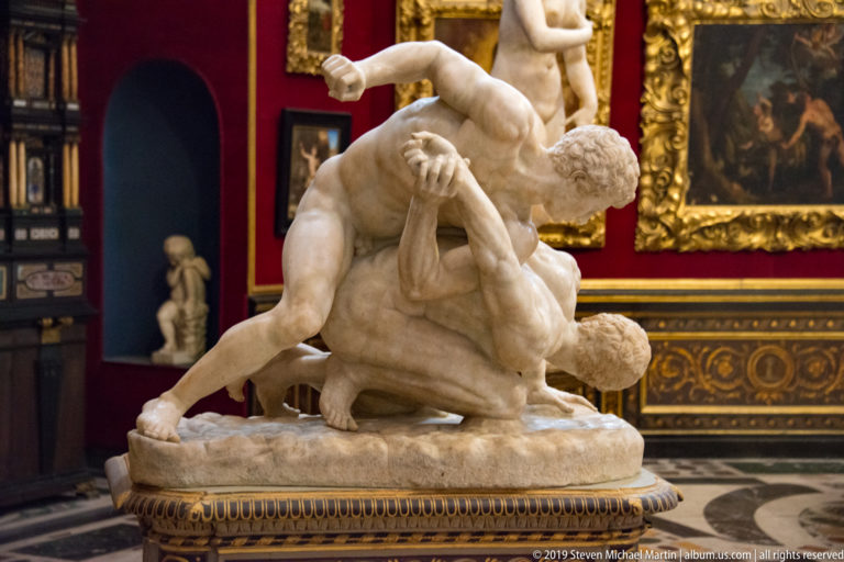 Two nude marble wrestlers grapple on a low oval base, one twisting over and pinning the other.