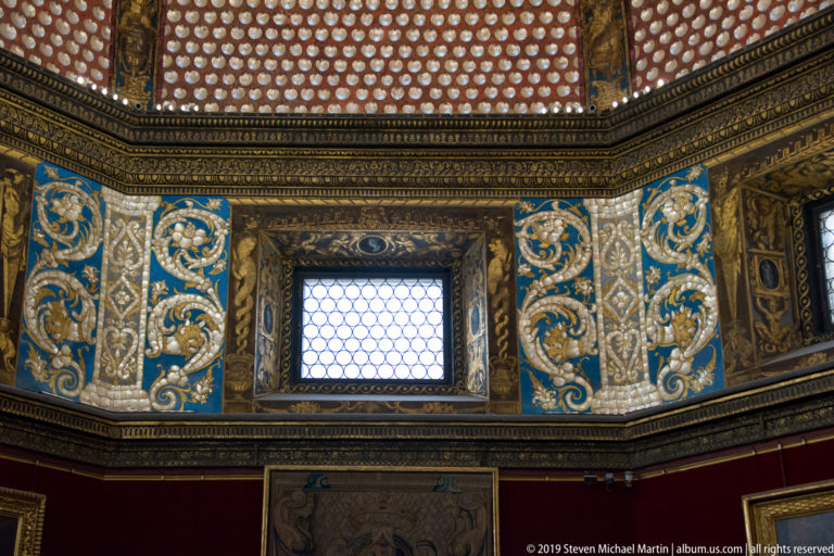 Blue-and-gold Tribuna wall panels and lattice window beneath a red dome densely covered with pale shell-like decoration.