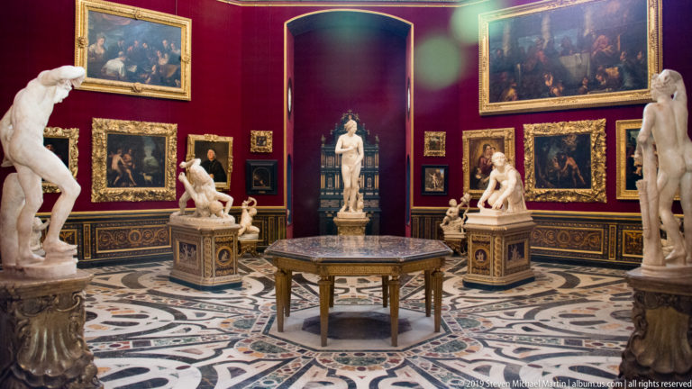 Octagonal Uffizi Tribuna with classical statues, gilded paintings, central table, red walls, and elaborate inlaid marble floor.
