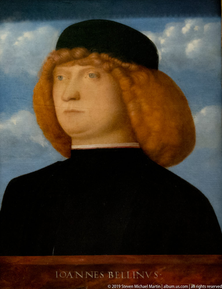Bust-length red-haired man in a black cap and garment above the painted inscription IOANNES BELLINI.