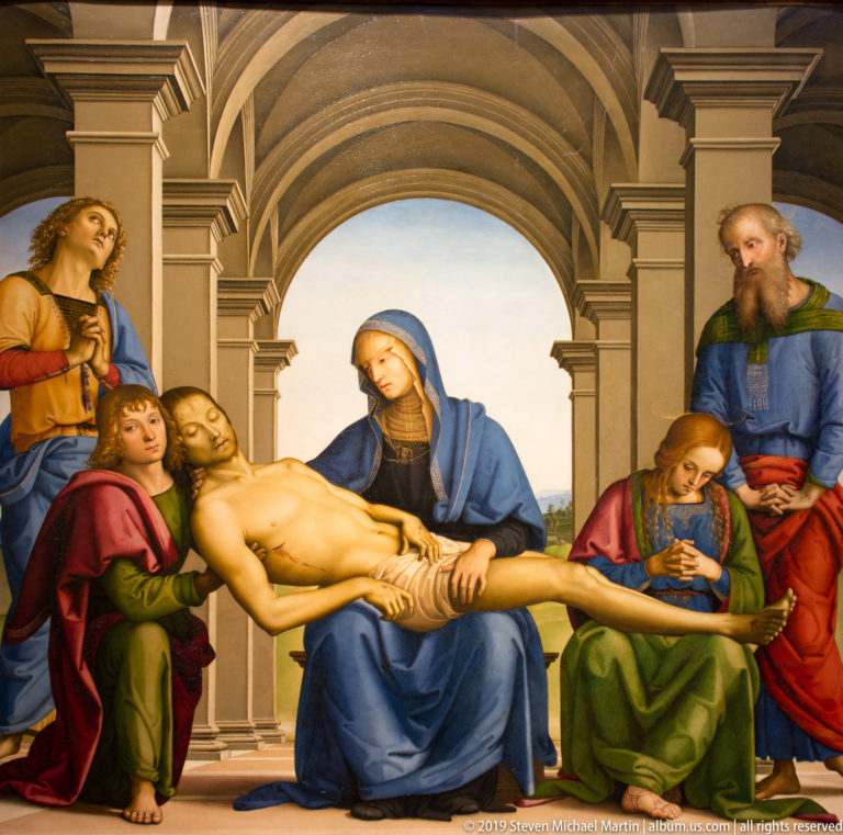 Dead Christ rests across the Virgin’s lap beneath a large arch, surrounded by grieving figures.